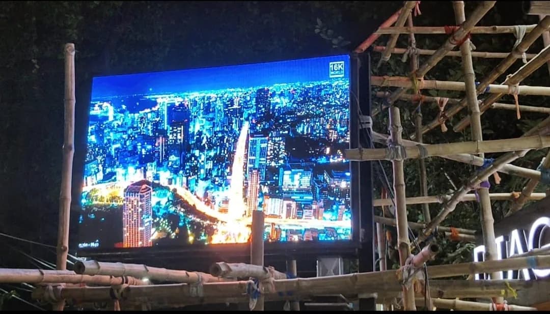 Outdoor LED screen at night showing a city skyline, with bamboo scaffolding beside it