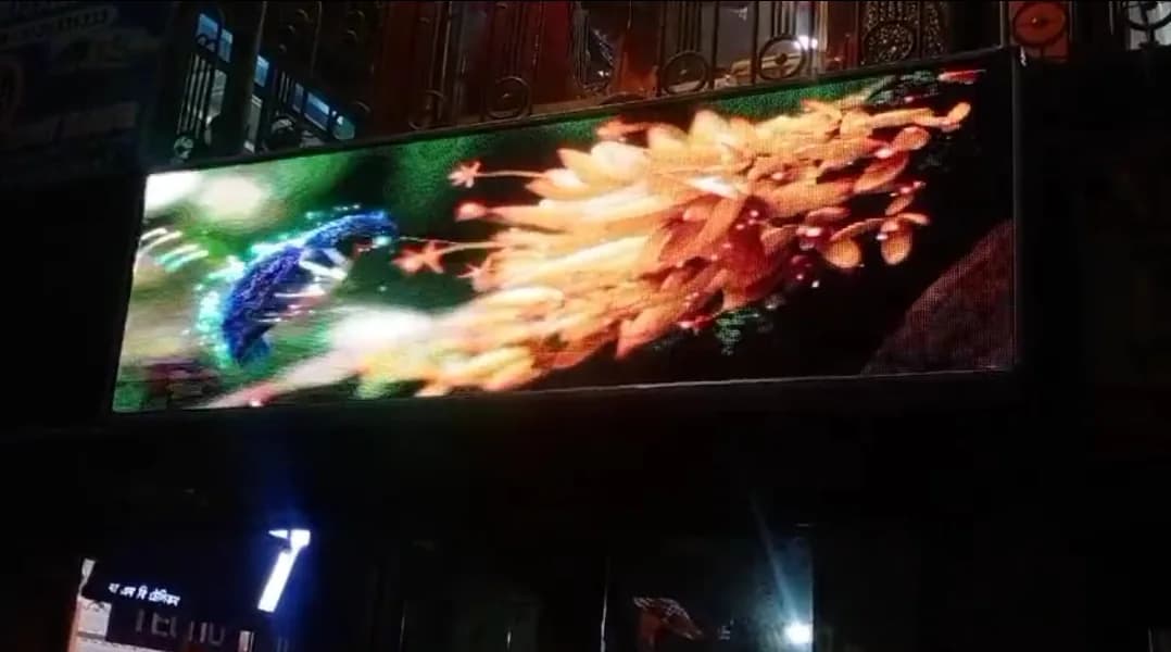 Wide outdoor LED screen at night showing colourful flowers above a shopfront