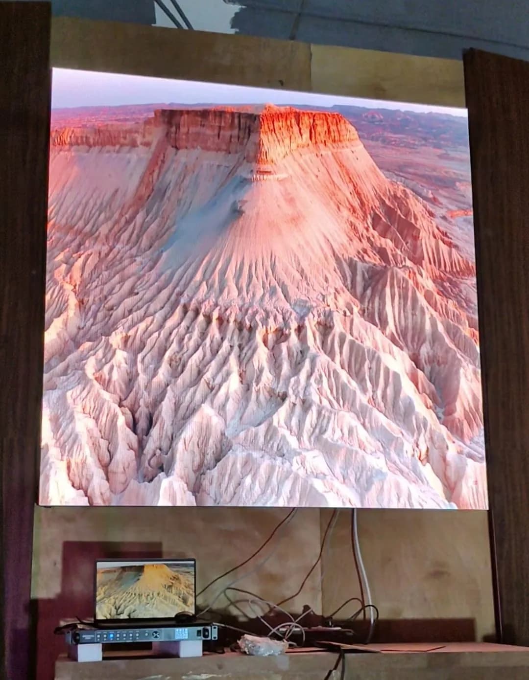 Indoor LED wall showing a desert landscape, with a laptop and video controller on a shelf below
