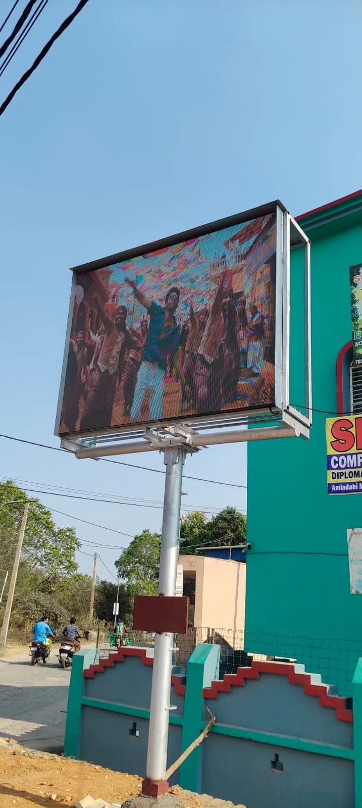 Pole-mounted outdoor LED screen in daylight beside a green building, showing a dance scene