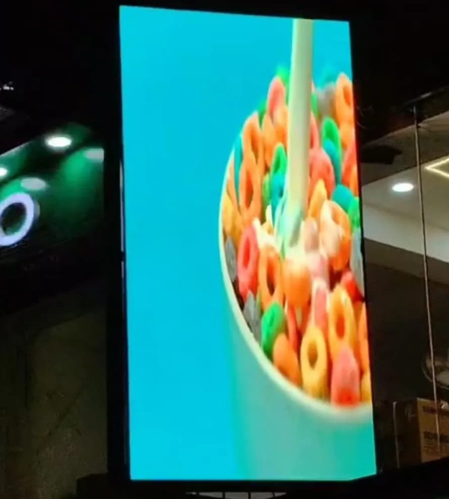 Vertical outdoor LED screen above a storefront at night showing a bowl of cereal
