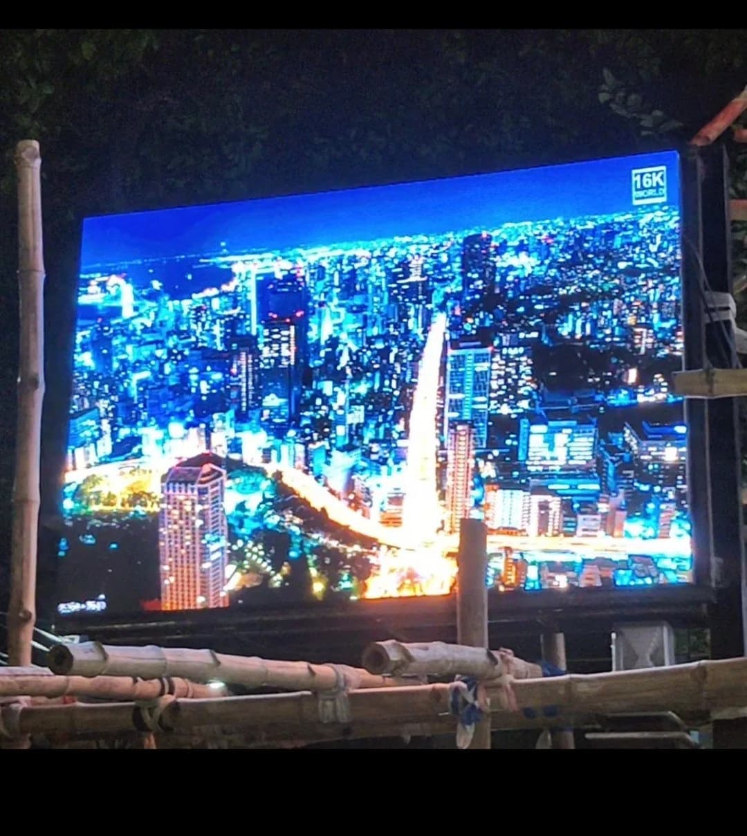 Outdoor LED screen at night showing a city skyline, held in a bamboo frame