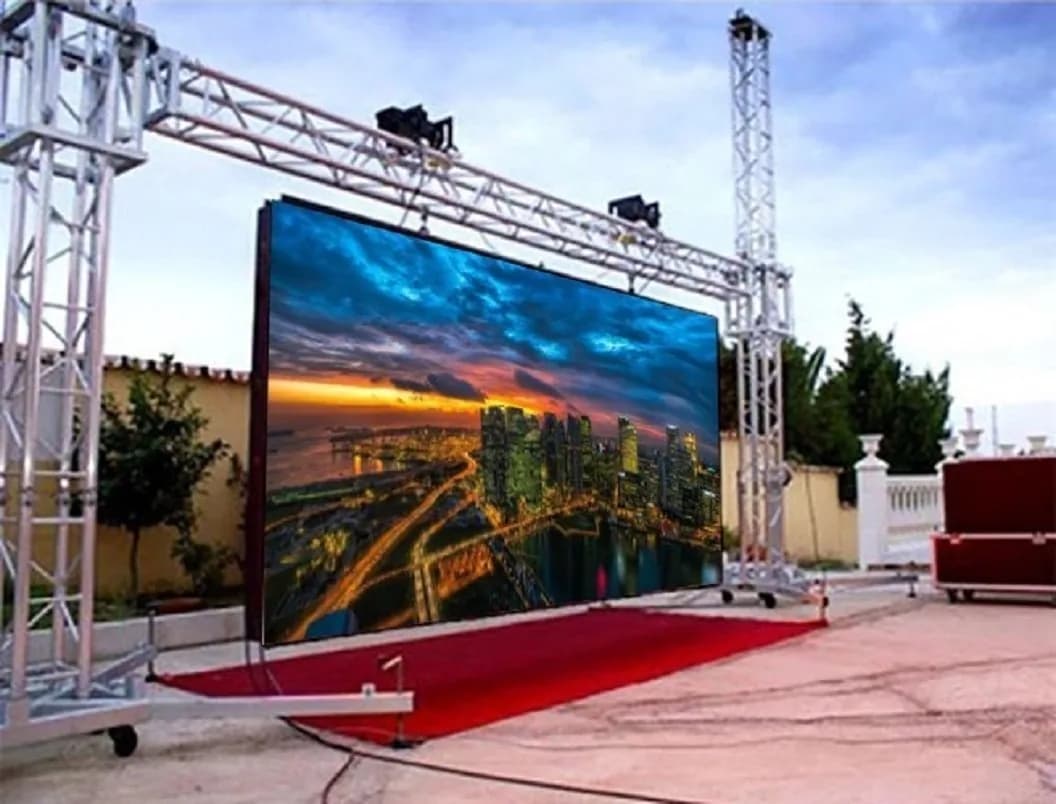 Outdoor LED screen on a truss over a red carpet, showing a city at sunset